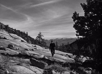 Movie still from “Out of the Past” (1947), directed by Jacques Tourneur – A man walking on a rocky hillside near a tree; Extreme Wide shot, High angle