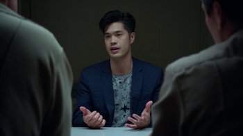 Movie still from “13 Reasons Why” (2017), created by Brian Yorkey – A man sitting at a table with his hands in front of him; Medium shot, Over the shoulder angle