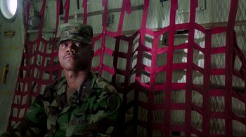 Movie still from “Outbreak” (1995), directed by Wolfgang Petersen – A man in fatigues is sitting in front of red chairs; Medium shot, Low angle