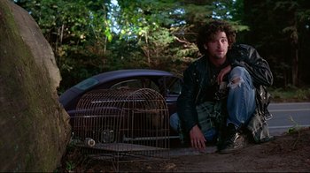Movie still from “Outbreak” (1995), directed by Wolfgang Petersen – A man sitting on the ground next to an old car; Medium shot, Low angle