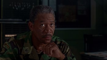 Movie still from “Outbreak” (1995), directed by Wolfgang Petersen – An older man in a military uniform is looking at the camera with his hand under his chin; Close Up shot, Over the shoulder angle