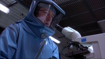 Movie still from “Outbreak” (1995), directed by Wolfgang Petersen – A man wearing a blue suit and a face mask; Close Up shot, Low angle