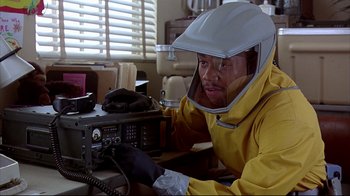 Movie still from “Outbreak” (1995), directed by Wolfgang Petersen – A man in a yellow raincoat is fixing a radio; Medium shot, Over the shoulder angle