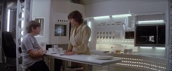 Movie still from “Outland” (1981), directed by Peter Hyams – A woman standing at a counter in a kitchen; Medium shot, Over the shoulder angle