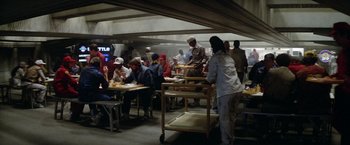 Movie still from “Outland” (1981), directed by Peter Hyams – A group of people sitting at tables in a kitchen; Wide shot, Over the shoulder angle