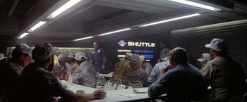 Movie still from “Outland” (1981), directed by Peter Hyams – A group of people sitting at tables in a room; Wide shot, Over the shoulder angle