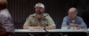 Movie still from “Outland” (1981), directed by Peter Hyams – A man sitting at a table wearing a white hat; Medium shot, Over the shoulder angle