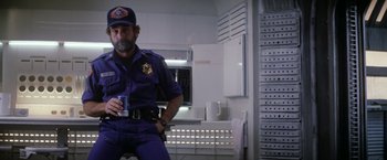 Movie still from “Outland” (1981), directed by Peter Hyams – A man in a uniform holding a cup in a room; Medium shot, Low angle