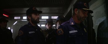 Movie still from “Outland” (1981), directed by Peter Hyams – A group of men standing next to each other in a room; Medium shot, Over the shoulder angle