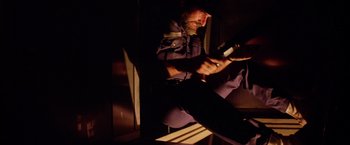 Movie still from “Outland” (1981), directed by Peter Hyams – A man sitting on a chair holding a cell phone; Medium shot, Low angle