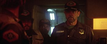 Movie still from “Outland” (1981), directed by Peter Hyams – A man in a uniform and a man in a hat; Medium shot, Over the shoulder angle
