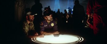 Movie still from “Outland” (1981), directed by Peter Hyams – A group of people sitting around a table; Medium shot, Over the shoulder angle