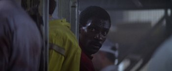 Movie still from “Outland” (1981), directed by Peter Hyams – A man in a red shirt and a yellow rain jacket; Close Up shot, Over the shoulder angle