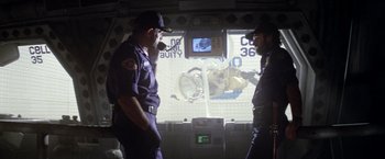 Movie still from “Outland” (1981), directed by Peter Hyams – Two police officers standing next to each other in front of a window; Wide shot, Low angle