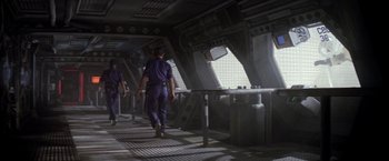 Movie still from “Outland” (1981), directed by Peter Hyams – Two people walking in a room with a window; Wide shot, High angle