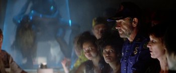 Movie still from “Outland” (1981), directed by Peter Hyams – A group of people standing in front of a projector screen; Medium shot, Over the shoulder angle