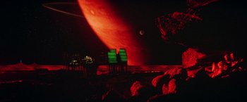 Movie still from “Outland” (1981), directed by Peter Hyams – A red planet with two green chairs in front of it; Extreme Wide shot, Low angle
