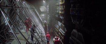 Movie still from “Outland” (1981), directed by Peter Hyams – A group of people in a warehouse with boxes on the shelves; Extreme Wide shot, High angle