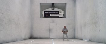 Movie still from “Outland” (1981), directed by Peter Hyams – A man standing in front of a wall holding a tennis racquet; Wide shot, Overhead angle