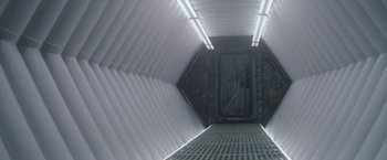 Movie still from “Outland” (1981), directed by Peter Hyams – An empty hallway with a door open and lights on; Wide shot, Overhead angle