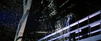 Movie still from “Outland” (1981), directed by Peter Hyams – A person standing on a metal staircase in front of a building; Extreme Wide shot, Low angle