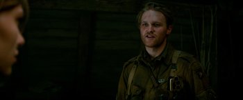 Movie still from “Overlord” (2018), directed by Julius Avery – A man in a military uniform standing in front of a wooden wall; Close Up shot, Low angle