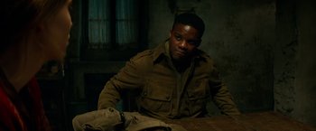 Movie still from “Overlord” (2018), directed by Julius Avery – A man sitting at a wooden table in a room; Medium shot, High angle
