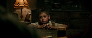 Movie still from “Overlord” (2018), directed by Julius Avery – A boy sitting at a wooden table in a dark room; Close Up shot, Over the shoulder angle