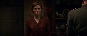 Movie still from “Overlord” (2018), directed by Julius Avery – A woman in a red shirt standing in front of a wall; Medium shot, Over the shoulder angle