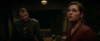 Movie still from “Overlord” (2018), directed by Julius Avery – A woman sitting at a table with a man standing next to her; Close Up shot, Over the shoulder angle
