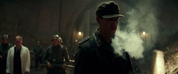 Movie still from “Overlord” (2018), directed by Julius Avery – A man in a military uniform smoking a cigarette; Medium shot, Low angle