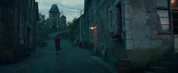 Movie still from “Overlord” (2018), directed by Julius Avery – A woman walking down a street near a brick building; Extreme Wide shot, High angle