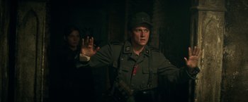 Movie still from “Overlord” (2018), directed by Julius Avery – A man in a military uniform is holding his hand up; Medium shot, Over the shoulder angle