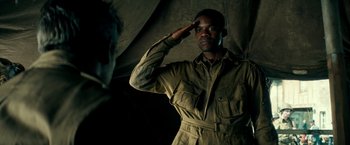 Movie still from “Overlord” (2018), directed by Julius Avery – A man saluting while wearing an army uniform; Medium shot, Over the shoulder angle