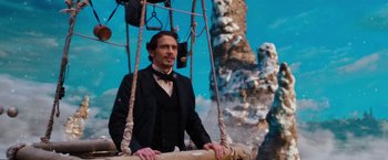 Movie still from “Oz the Great and Powerful” (2013), directed by Sam Raimi – A man wearing a suit and tie standing on top of a swing; Medium shot, Low angle