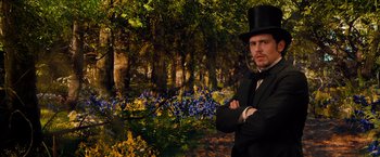 Movie still from “Oz the Great and Powerful” (2013), directed by Sam Raimi – A man wearing a top hat standing next to a forest; Medium shot, Low angle