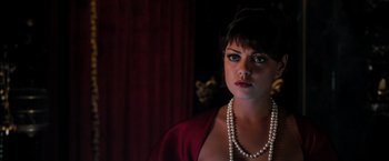 Movie still from “Oz the Great and Powerful” (2013), directed by Sam Raimi – A woman wearing a red dress and pearls in a dark room; Close Up shot, Over the shoulder angle