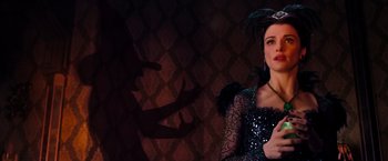 Movie still from “Oz the Great and Powerful” (2013), directed by Sam Raimi – A woman in a black dress holding a microphone; Medium shot, Over the shoulder angle
