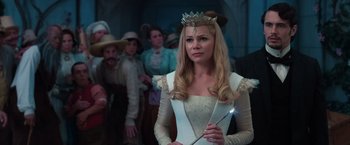 Movie still from “Oz the Great and Powerful” (2013), directed by Sam Raimi – A woman in a white dress and a crown holding a wand in front of a group of people; Medium shot, Over the shoulder angle