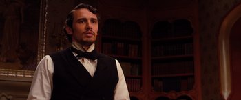 Movie still from “Oz the Great and Powerful” (2013), directed by Sam Raimi – A man wearing a vest and bow tie in a library; Medium shot, Low angle