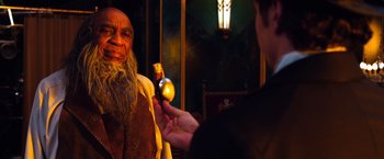 Movie still from “Oz the Great and Powerful” (2013), directed by Sam Raimi – A man holding a bottle of wine in front of an older man; Close Up shot, Over the shoulder angle
