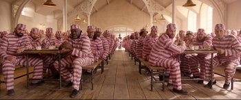 Movie still from “Paddington 2” (2017), directed by Paul King – A group of men in pink and white striped suits sitting on benches; Wide shot, High angle