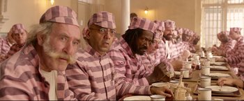 Movie still from “Paddington 2” (2017), directed by Paul King – A group of men in pink and white striped pajamas eating; Medium shot, High angle