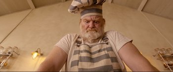 Movie still from “Paddington 2” (2017), directed by Paul King – An old man with a beard wearing an apron and a chef's hat; Close Up shot, Overhead angle