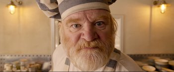 Movie still from “Paddington 2” (2017), directed by Paul King – An old man with a beard wearing an apron and a hat; Close Up shot, Low angle