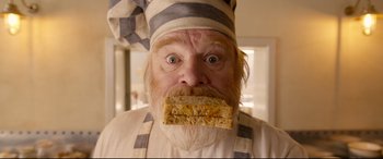 Movie still from “Paddington 2” (2017), directed by Paul King – An old man with a beard and a mustache with a piece of cake in his mouth; Extreme Close Up shot, Low angle