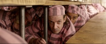 Movie still from “Paddington 2” (2017), directed by Paul King – A man in pink and black striped pajamas hiding under a table; Medium shot, High angle