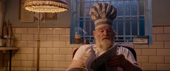 Movie still from “Paddington 2” (2017), directed by Paul King – An old man wearing a chef's hat while reading a newspaper; Close Up shot, Over the shoulder angle