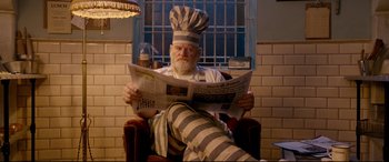 Movie still from “Paddington 2” (2017), directed by Paul King – An old man wearing a chef's hat while reading a newspaper; Medium shot, Low angle