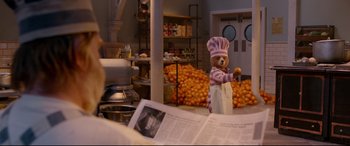 Movie still from “Paddington 2” (2017), directed by Paul King – A teddy bear dressed as a chef in front of a bunch of oranges in a kitchen; Wide shot, Over the shoulder angle